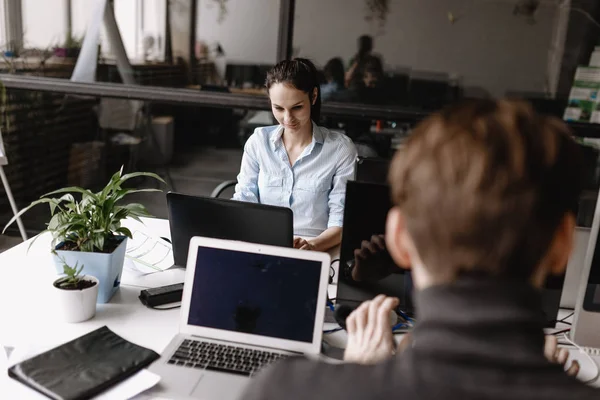 Ung kvinne og mann kledd i kontorklær jobber på bærbare datamaskiner som sitter på pulter i det moderne kontoret utstyrt med moderne kontorutstyr. – stockfoto