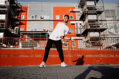 Kot giyinmiş ve t-shirt genç adam sıcak gün kentsel binaların arka planda sokakta modern dans dans ediyor