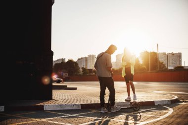 Scooter ve kız ile genç şık adam güneşli gün Park için meydanda birlikte ayakta