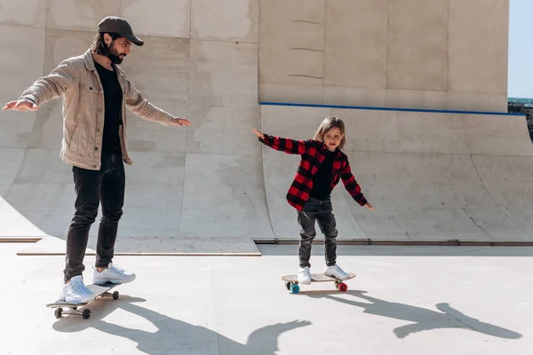 Padre y su hijo pequeño vestidos con ropa casual montan skateboards en un parque de skate con toboganes afuera en el día soleado —  Fotos de Stock