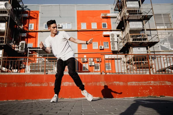 Ung kille klädd i jeans och t-shirt dansar modern dans på gatan på bakgrunden av urbana byggnader i den varma dagen — Stockfoto