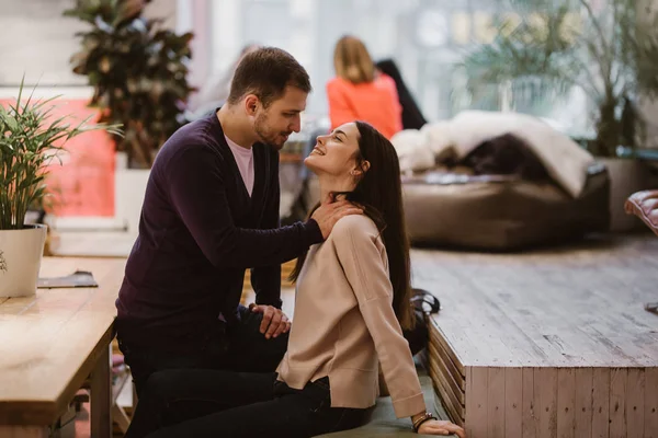 Glücklicher liebevoller Kerl legt seine Hände auf die Schultern der Mädchen, die am Tisch im Café sitzen und schaut sie an — Stockfoto