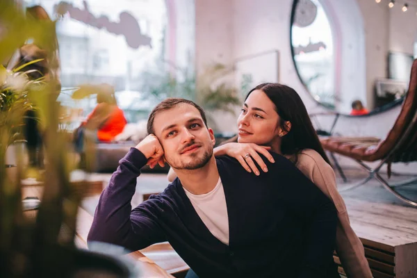 Liebende Mädchen hält ihre Hand auf der Schulter ihres Freundes, der am Tisch im gemütlichen romantischen Café sitzt — Stockfoto