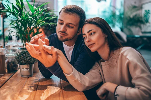 Glücklich liebender Kerl hält seine Freundinnen an der Hand, die am Tisch im Café sitzen und schaut sie an. — Stockfoto