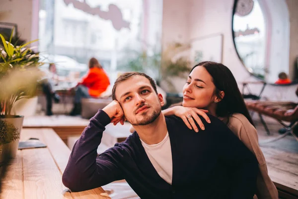 Liebende Mädchen hält ihre Hand auf der Schulter ihres Freundes, der am Tisch im gemütlichen romantischen Café sitzt — Stockfoto