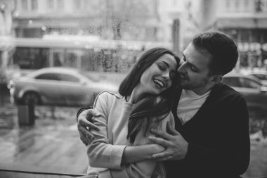 Loving adam rahat bir kafede pencere üzerinde oturan onun güzel mutlu kız arkadaşı kucaklar. Siyah beyaz fotoğraf