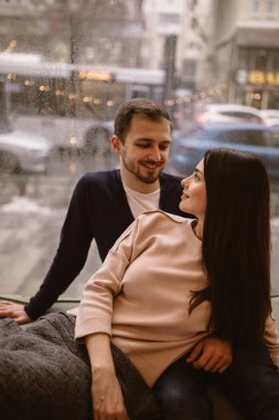 Sevgi dolu mutlu bir çift. Adam ve kız arkadaşı rahat bir kafede pencere üzerinde birbirlerine yakın oturan kazak ve kot giymiş.