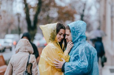 Romantik sevgi dolu çift, adam ve yağmurluk kız arkadaşı yağmurda sokakta yüz yüze durmak