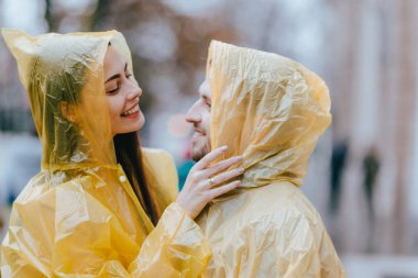 Mutlu sevgi dolu çift, adam ve sarı yağmurluklar giymiş kız arkadaşı yağmurda sokakta sarılmak vardır