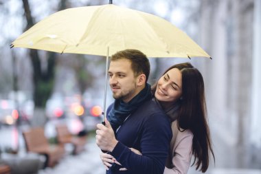 Mutlu romantik çift, adam ve rahat giysiler giymiş kız arkadaşı şemsiye altında sarılma ve yağmurda sokakta birbirlerine bakmak.