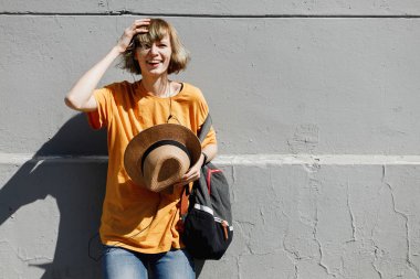 Sarı bir tişört giymiş genç kız elinde bir saman şapka tutan bir yaz güneşli bir gün bir şehir sokakta gri bir binada eğiliyor standları