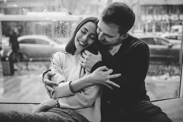 Vackert par. Kärleksfull kille kramar hans charmiga flickvän sitter på fönsterbrädan i ett mysigt kafé. Svartvitt foto — Stockfoto