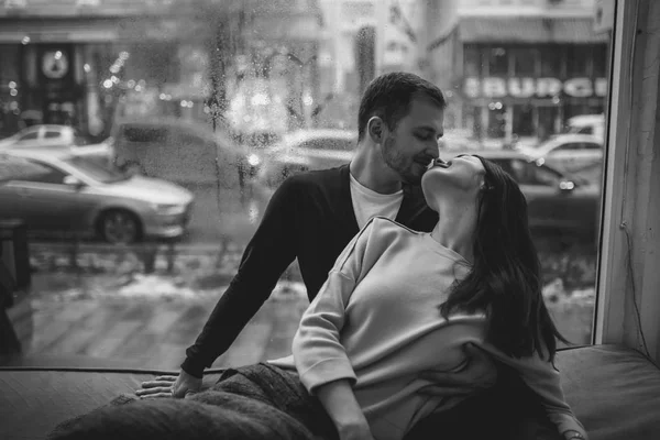 Romantisches Paar. Liebender Kerl küsst seine schöne Freundin, die auf der Fensterbank in einem gemütlichen Café sitzt. Schwarz-Weiß-Foto — Stockfoto