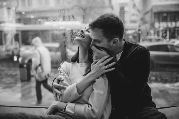 Hermosa pareja. El chico cariñoso abraza a su encantadora novia sentada en el alféizar de la ventana en un acogedor café. Foto en blanco y negro —  Fotos de Stock