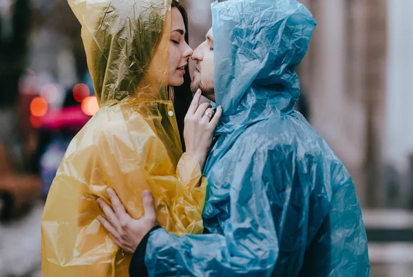 Cara amorosa e sua namorada nas capas de chuva ficar cara a cara na rua na chuva — Fotografia de Stock