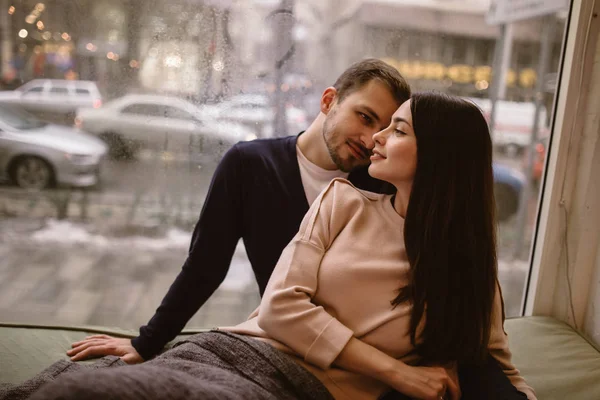 Szerető pár. Guy és barátnője öltözött a pulóverek és a farmer ül közel egymáshoz az ablakpárkányon egy hangulatos kávézóban. — Stock Fotó