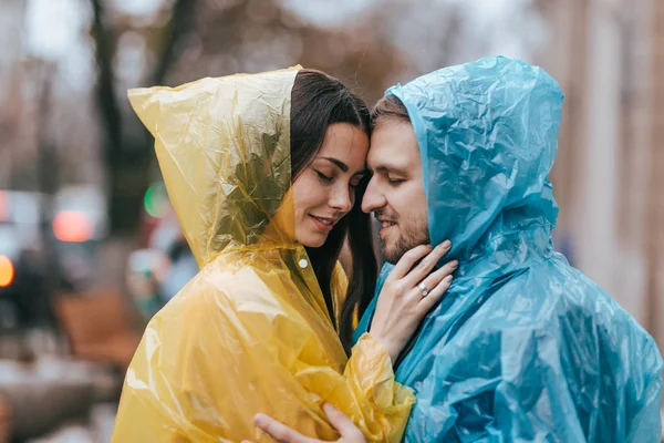 Romantico amorevole coppia, ragazzo e la sua ragazza in impermeabili stand faccia a faccia sulla strada sotto la pioggia — Foto Stock