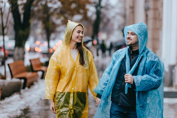 Amare ragazzo e ragazza in impermeabili gialli e blu camminare per strada sotto la pioggia — Foto Stock