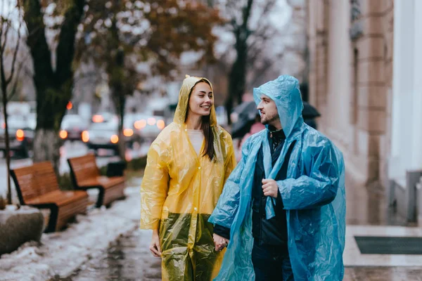 Cara e menina amorosa nas capas de chuva amarelas e azuis ficar na rua na chuva — Fotografia de Stock