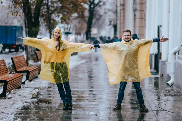 Amante cara e menina vestida com capas de chuva amarelas stand na rua na chuva — Fotografia de Stock