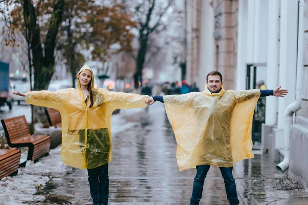 Loving ragazzo e ragazza vestita con impermeabili gialli stand sulla strada sotto la pioggia — Foto Stock