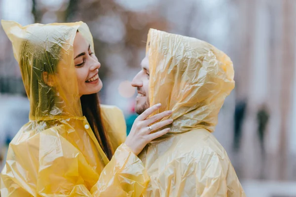 Happy loving couple, guy and his girlfriend dressed in yellow raincoats are hugging on the street in the rain