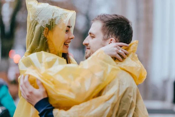Romantica coppia amorevole, ragazzo e la sua ragazza vestita con impermeabili gialli si abbracciano per strada sotto la pioggia — Foto Stock