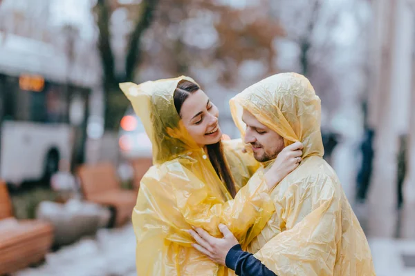 Coppia amorevole, ragazzo e la sua ragazza vestita con impermeabili gialli si abbracciano per strada sotto la pioggia — Foto Stock