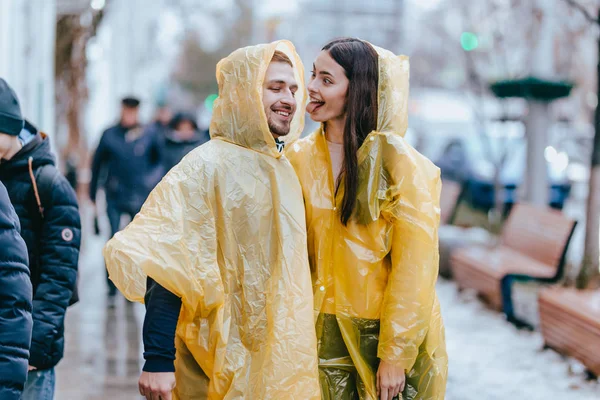 Happy guy and his girlfriend dressed in yellow raincoats are walking on the street in the rain