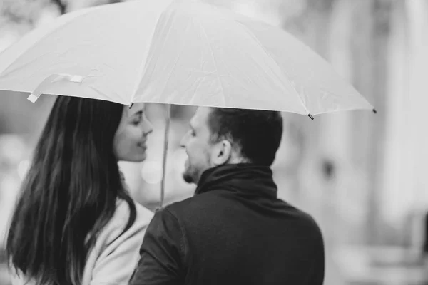 Bella coppia, ragazzo e la sua ragazza vestita con abiti casual stare sotto l'ombrello e guardarsi per strada sotto la pioggia. Foto in bianco e nero — Foto Stock