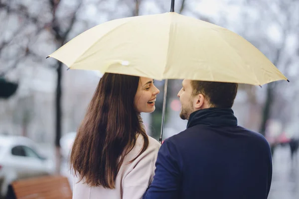 Belo casal feliz, cara e sua namorada vestida com roupas casuais ficar sob o guarda-chuva e olhar um para o outro na rua na chuva — Fotografia de Stock