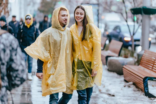 Guy e sua namorada vestidos com capas de chuva amarelas estão andando na rua na chuva — Fotografia de Stock