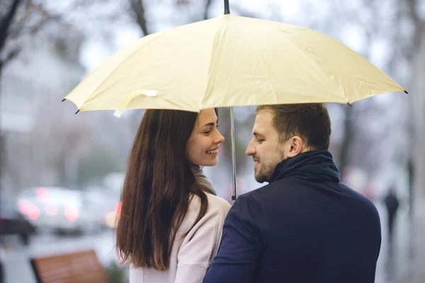 Feliz casal romântico, cara e sua namorada vestida com roupas casuais andar sob o guarda-chuva e olhar um para o outro na rua na chuva . — Fotografia de Stock