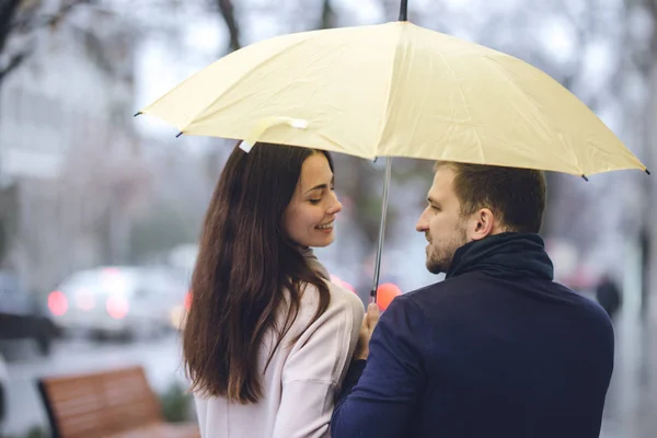 Lycklig romantiskt par, Guy och hans flickvän klädd i casual kläder gå under paraplyet och titta på varandra på gatan i regnet. — Stockfoto