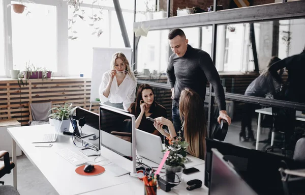 Unge hold arbejder ved et skrivebord med en computer og bærbare computere i et let moderne åbent rum kontor - Stock-foto