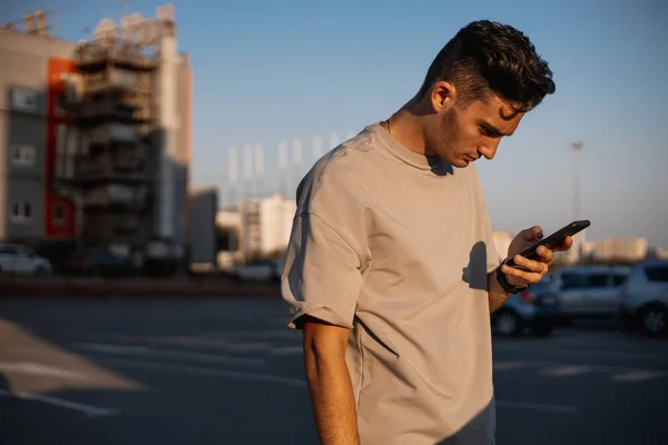 Jeune homme habillé en t-shirt blanc utilise le téléphone sur la place pour se garer le jour ensoleillé — Photo