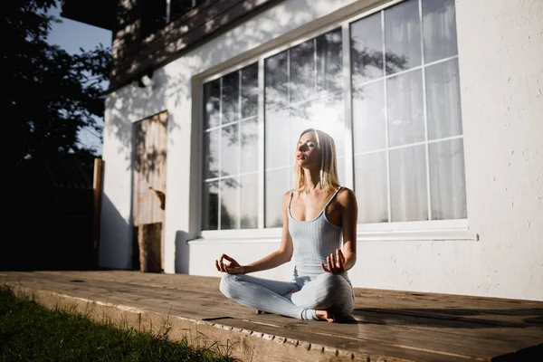 Genç kadın güneşli sabah dizlerinin üzerinde elleri ile bahçede ahşap bir podyum üzerinde lotus pozisyonda oturan yoga pratik
