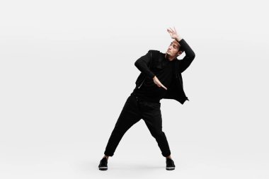Koyu saçlı şık bir adam şık siyah giysiler giymiş sokak dansı dans ediyor. Elleriyle stilize hareketler yapıyor.