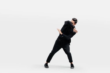 Koyu saçlı şık bir adam şık siyah giysiler giymiş sokak dansı dans ediyor. Elleriyle stilize hareketler yapıyor.