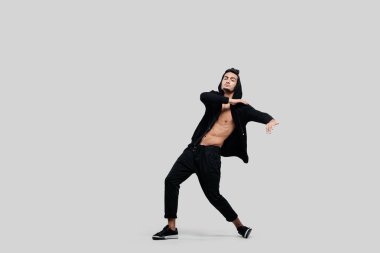 Yakışıklı genç dansçı dans Caddesi'nin siyah pantolon, çıplak bir gövde üzerinde bir kazak ve beyaz bir arka plan üzerinde başlık dans giymiş