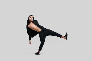 Siyah pantolon giymiş genç yakışıklı genç dansçı, çıplak gövde üzerinde bir sweatshirt sokak dansı dans ederken bir bacak yukarı kaldırır