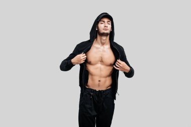Siyah pantolon giymiş şık genç dansçı, çıplak gövde üzerinde bir sweatshirt ve kap üzerinde bir başlık beyaz bir arka plan üzerinde duruyor