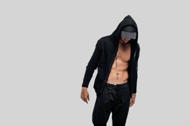 Yakışıklı genç dansçı kap ve siyah pantolon üzerinde bir başlık ile çıplak bir gövde üzerinde bir sweatshirt giymiş beyaz bir arka plan üzerinde duruyor