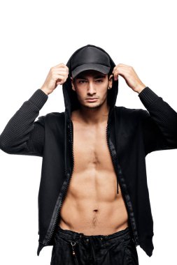Yakışıklı genç dansçı kap ve siyah pantolon üzerinde bir başlık ile çıplak bir gövde üzerinde bir sweatshirt giymiş beyaz bir arka plan üzerinde duruyor
