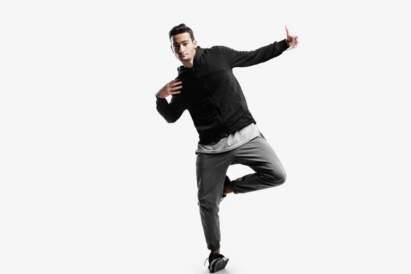 Elegante giovane uomo che indossa una felpa nera e pantaloni grigi sta ballando balli di strada su uno sfondo bianco — Foto Stock