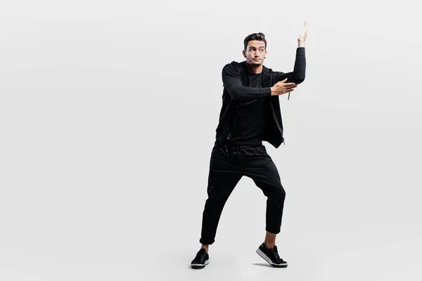 Jeune homme élégant aux cheveux bruns vêtu d'un élégant vêtement noir danse les danses de rue. Il fait des mouvements stylisés avec ses mains — Photo