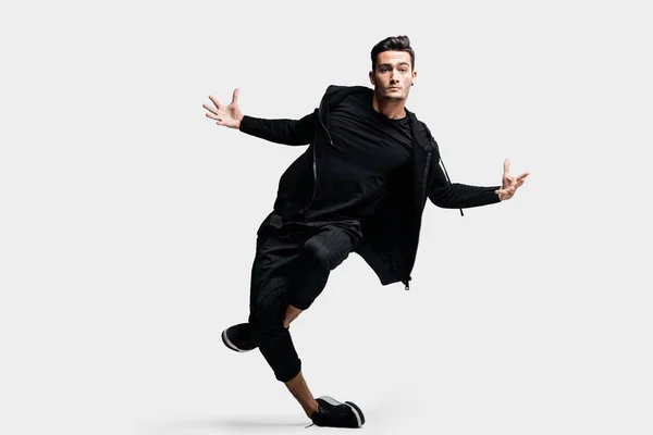 Dançarino jovem e elegante de cabelos escuros vestindo uma camisola preta e calças pretas faz movimentos estilizados de danças de rua — Fotografia de Stock