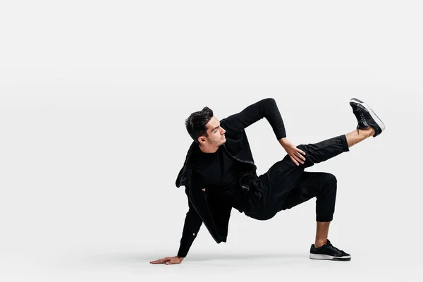 Beau jeune homme portant un sweat noir et un pantalon noir danse breakdance faire des mouvements de danse sur le sol — Photo