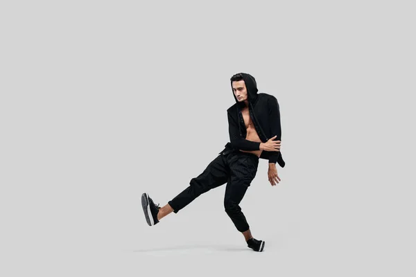 Ung snygg ung dansare klädd i svarta byxor, en sweatshirt på en naken torso lyfter ett ben upp medan Dancing Street Dance — Stockfoto
