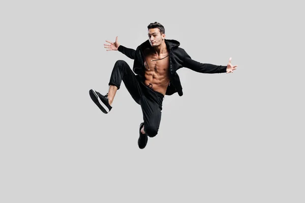 검은 바지 입은 거리 춤의 잘생긴 댄서와 벌 거 벗은 상체에 셔츠 점프 하 고 그의 양쪽에 팔을 확산 — 스톡 사진
